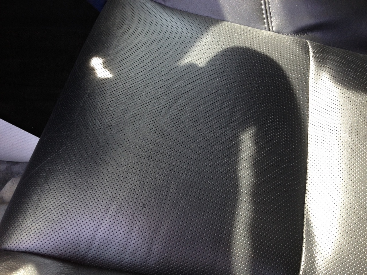 Close-up of repaired black perforated leather car seat upholstery.